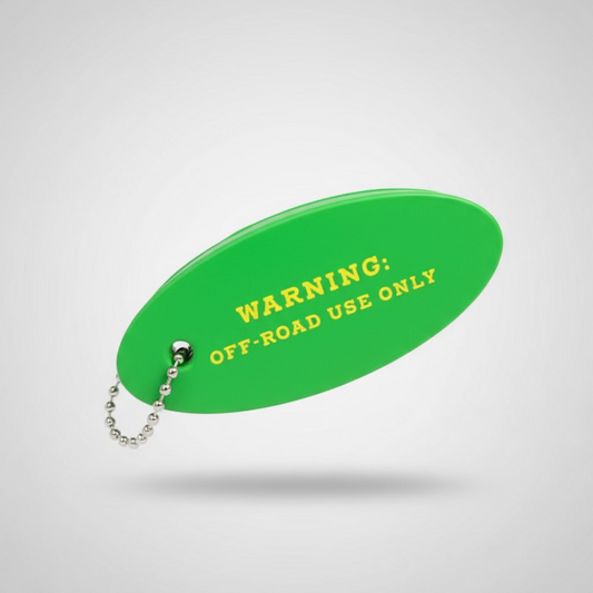 A bright green oval floating keychain with yellow text reading 'WARNING: OFF-ROAD USE ONLY' attached to a small silver ball chain, placed on a dark textured surface.