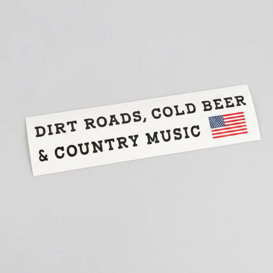 A white bumper sticker with black text reading 'DIRT ROADS, COLD BEER & COUNTRY MUSIC' and a small American flag graphic, placed on a dark tabletop.