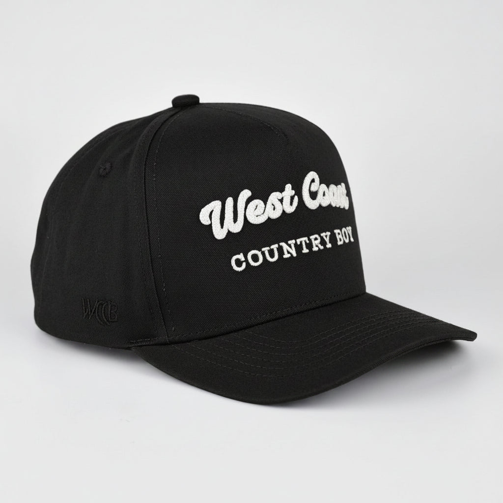 A Black baseball cap with 'West Coast COUNTRY BOY' embroidered in white on the front, shown on a light gray studio background.