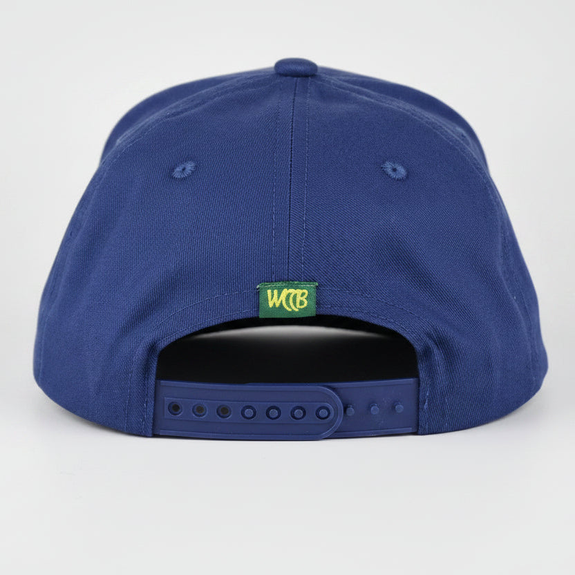 A royal blue snapback cap shown from the back, featuring a small green and yellow 'WCCB' logo patch and a dark gray plastic adjustment slider, set against a light gray studio background.