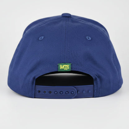 A royal blue snapback cap shown from the back, featuring a small green and yellow 'WCCB' logo patch and a dark gray plastic adjustment slider, set against a light gray studio background.