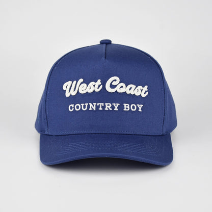 A royal blue baseball cap with 'West Coast COUNTRY BOY' embroidered in white on the front, set against a light gray studio background.