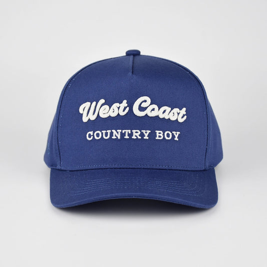 A royal blue baseball cap with 'West Coast COUNTRY BOY' embroidered in white on the front, set against a light gray studio background.