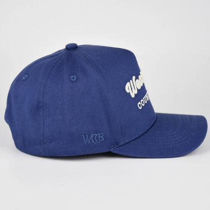 A royal blue baseball cap with white embroidered text on the side, photographed on a light gray studio background.