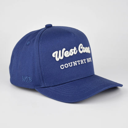 A royal blue baseball cap with 'West Coast COUNTRY BOY' embroidered in white on the front, shown on a light gray studio background.