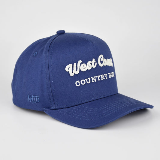 A royal blue baseball cap with 'West Coast COUNTRY BOY' embroidered in white on the front, shown on a light gray studio background.