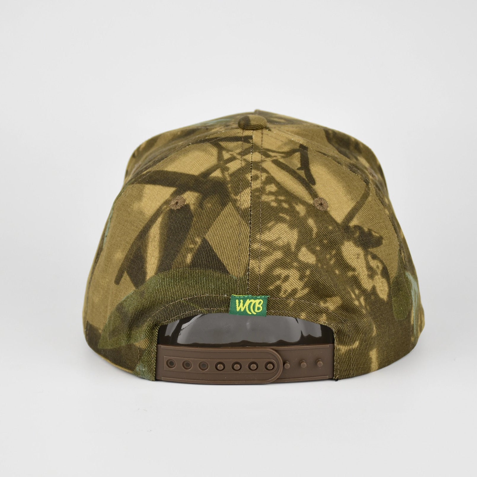 A camouflage baseball cap shown from the back, featuring a green and brown woodland camo pattern, a brown snapback closure, and a small green 'WCCB' brand patch.