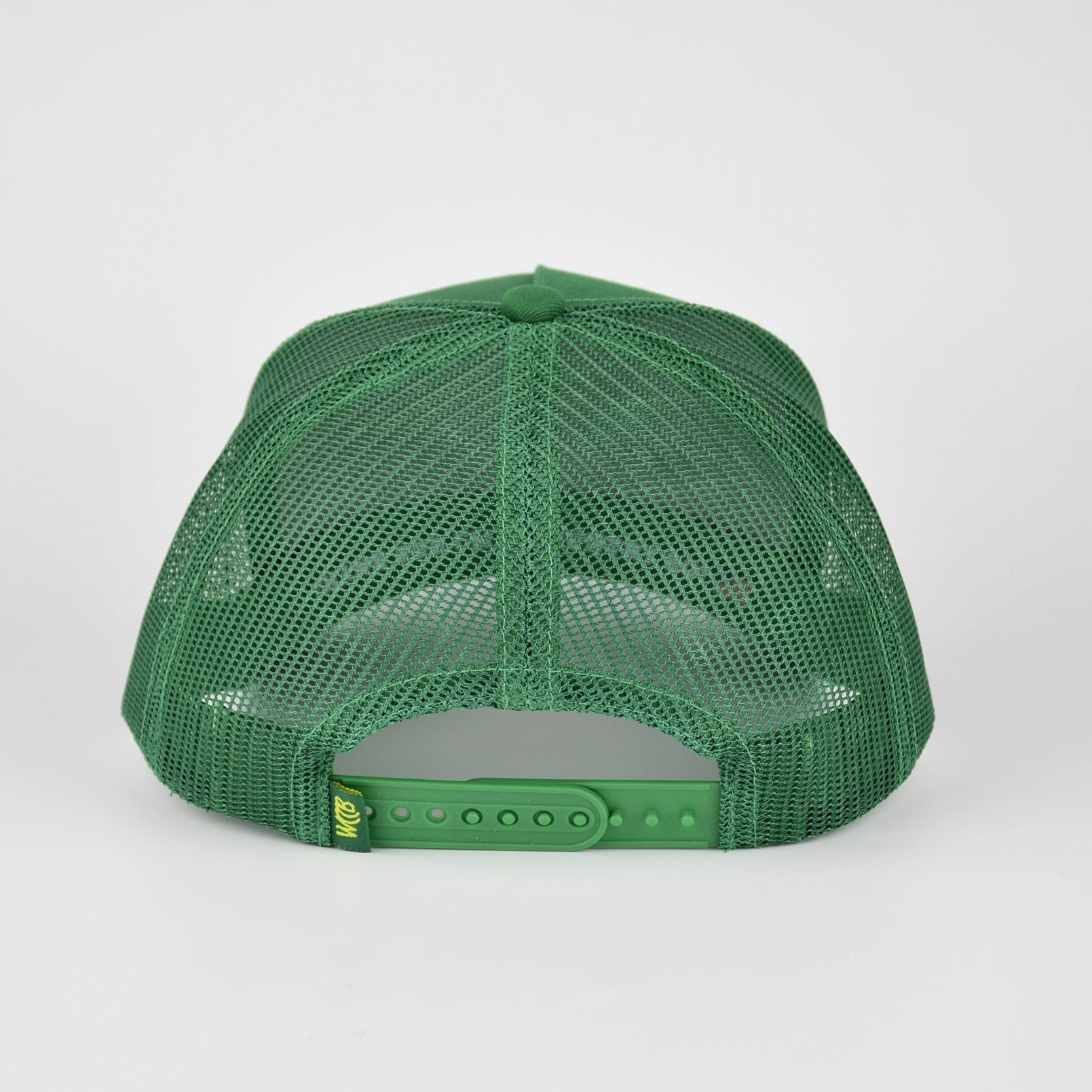 A green mesh-back trucker cap shown from the back, featuring a green fabric back and an adjustable snap closure, photographed against a light gray studio background.