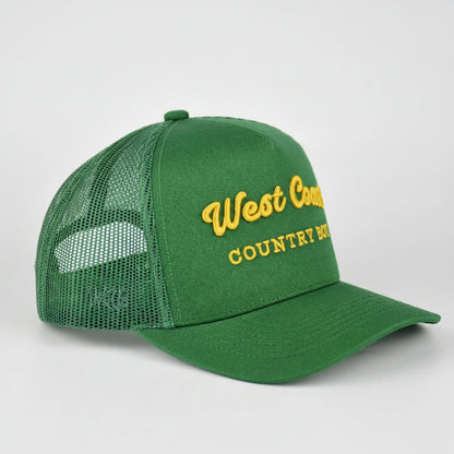 A green trucker-style baseball cap with a curved brim and mesh back, featuring yellow embroidered text on the front that reads 'West Country COUNTRY BOY.