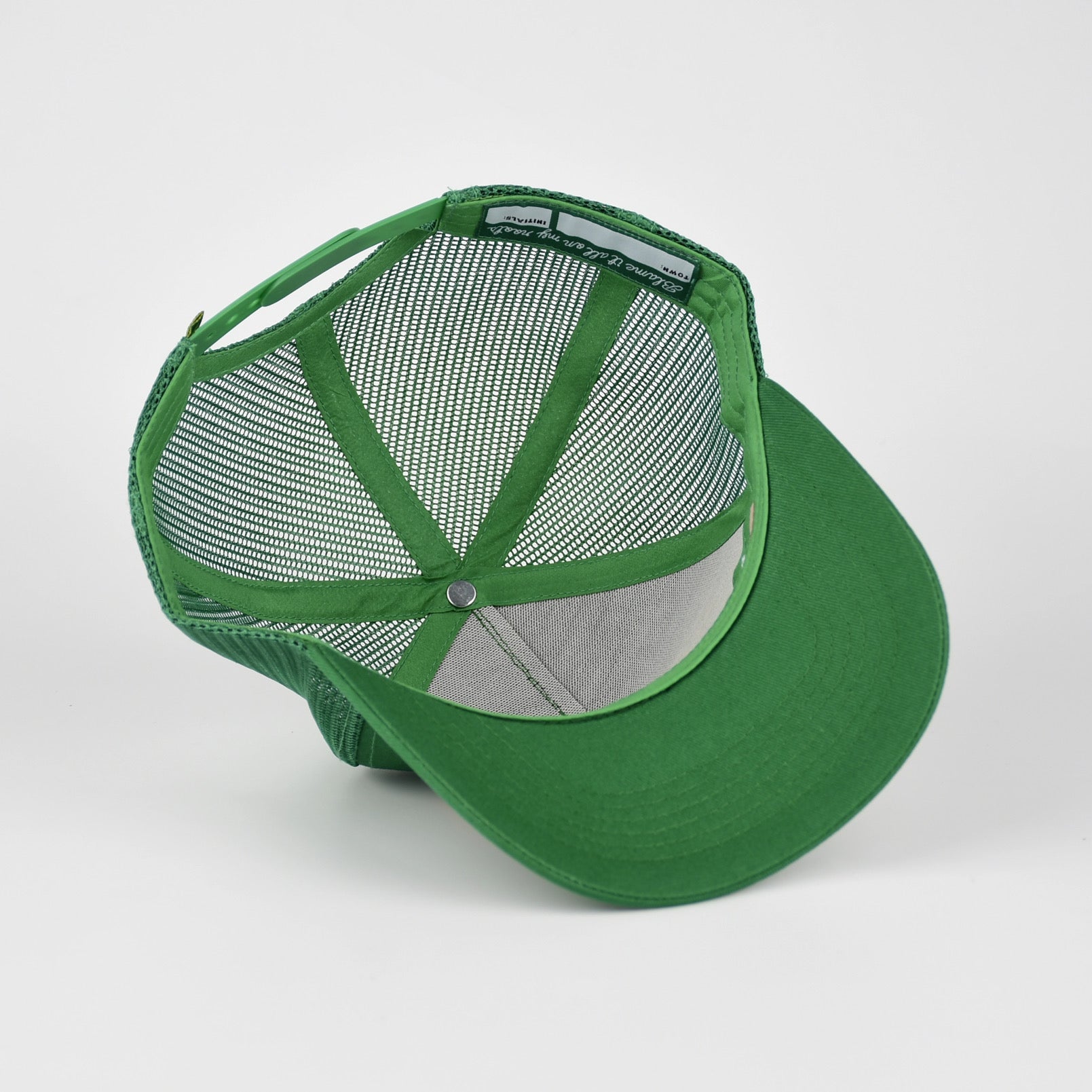 A green trucker-style cap with a solid green visor and green mesh back panels, shown from a three-quarters angle on a light gray background.