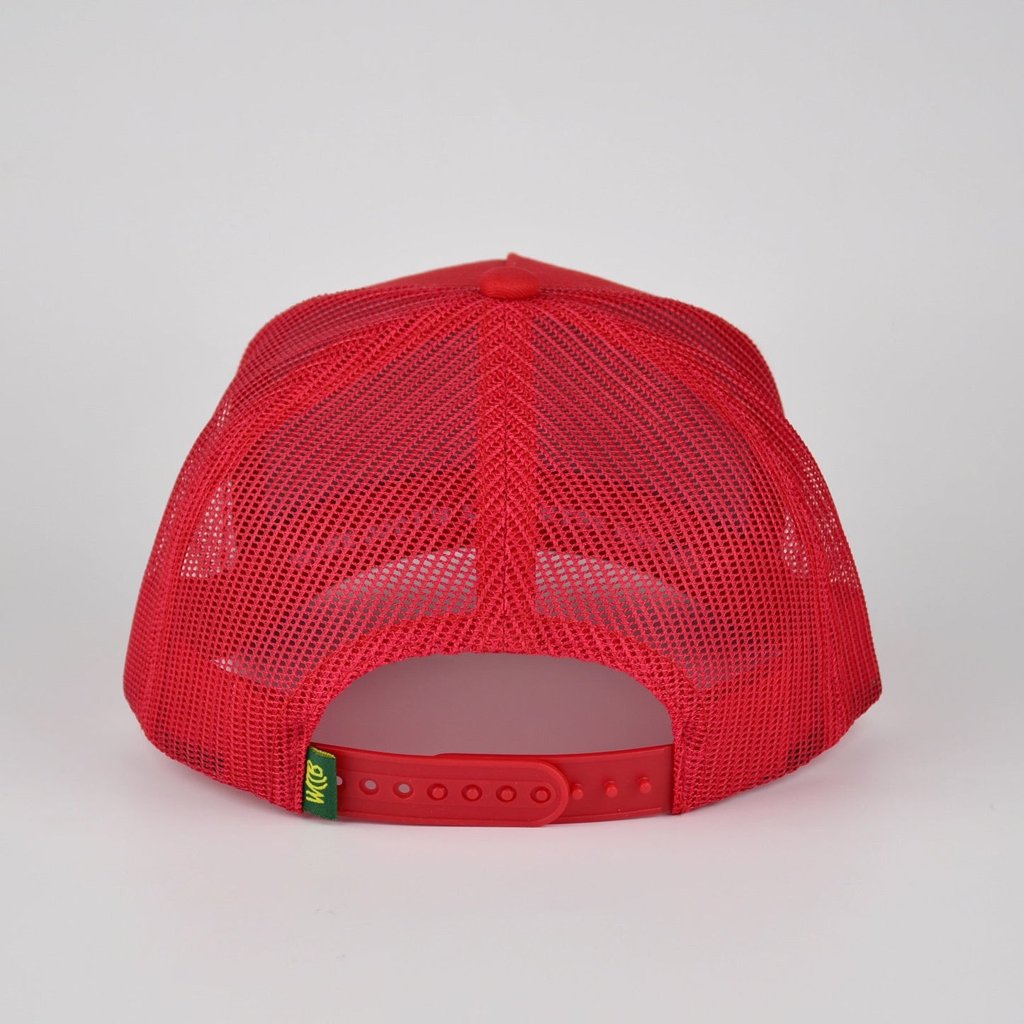 A red trucker-style mesh cap shown from the back, featuring a red fabric front panel, red mesh back, and an adjustable red snap closure with a small green and yellow WCCB tag.