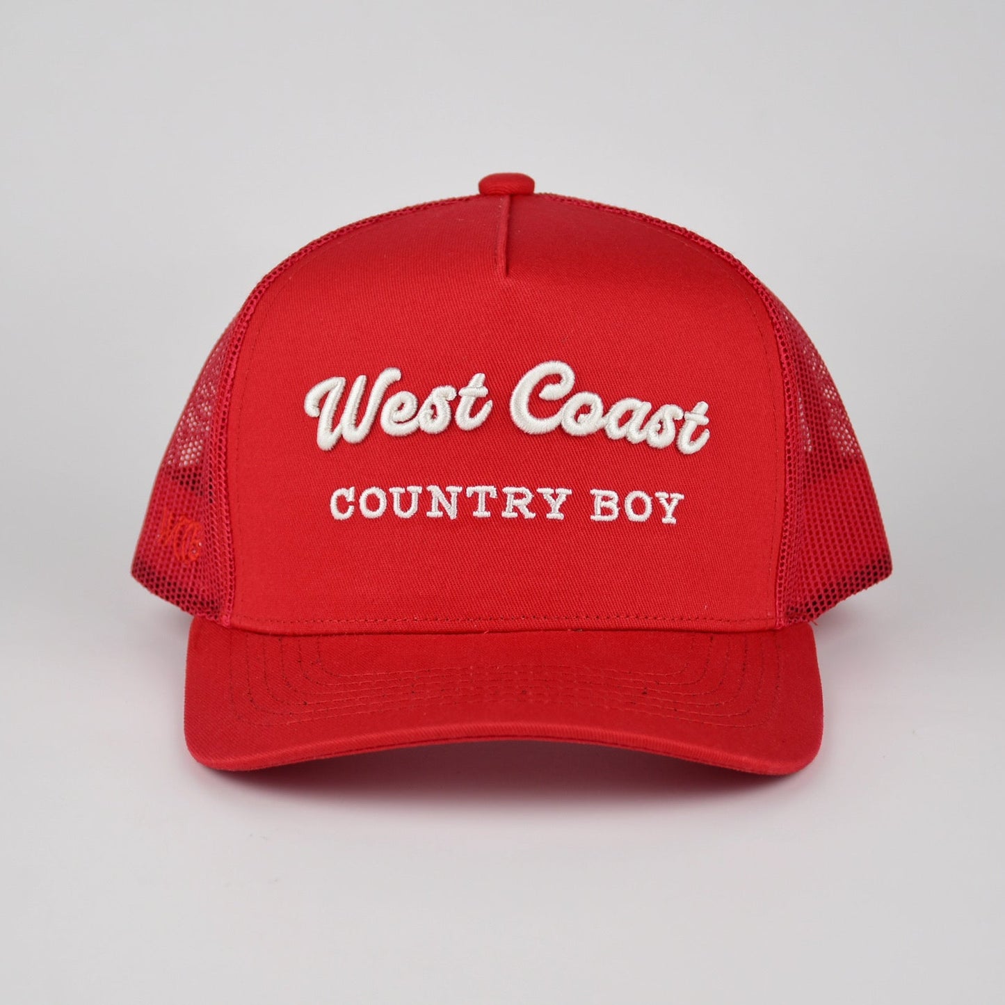 A red trucker-style cap with white embroidered text reading 'West Coast COUNTRY BOY' on the front, shown against a light gray studio background.