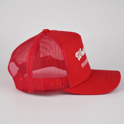 A red trucker-style baseball cap with a curved brim and red mesh back panels, featuring white embroidered text on the front side panel, WCCB on the side, shown against a light gray studio background.