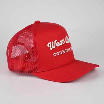 A red trucker-style baseball cap with white embroidered text reading 'West Coast COUNTRY BOY' on the front, shown on a light gray studio background.