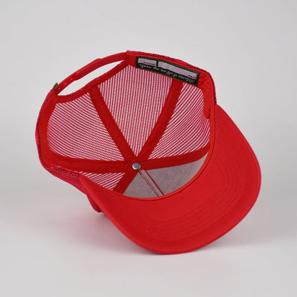A red trucker-style cap with a solid red curved brim and red mesh back panels, shown from a three-quarters angle on a light gray background.