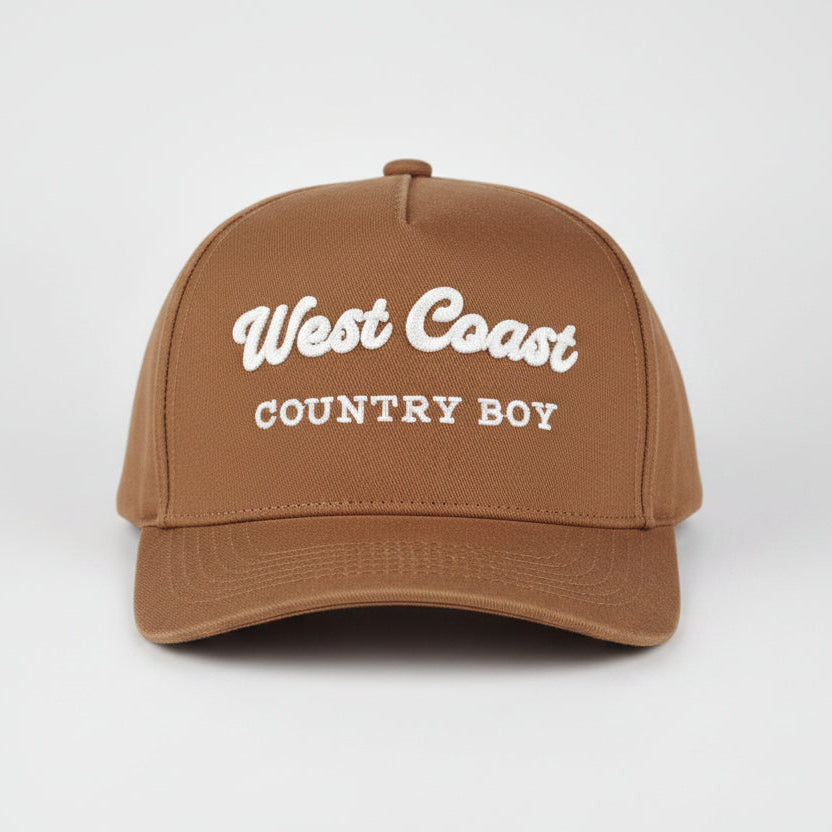 A royal blue baseball cap with 'West Coast COUNTRY BOY' embroidered in white on the front, set against a light gray studio background.