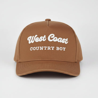 A royal blue baseball cap with 'West Coast COUNTRY BOY' embroidered in white on the front, set against a light gray studio background.