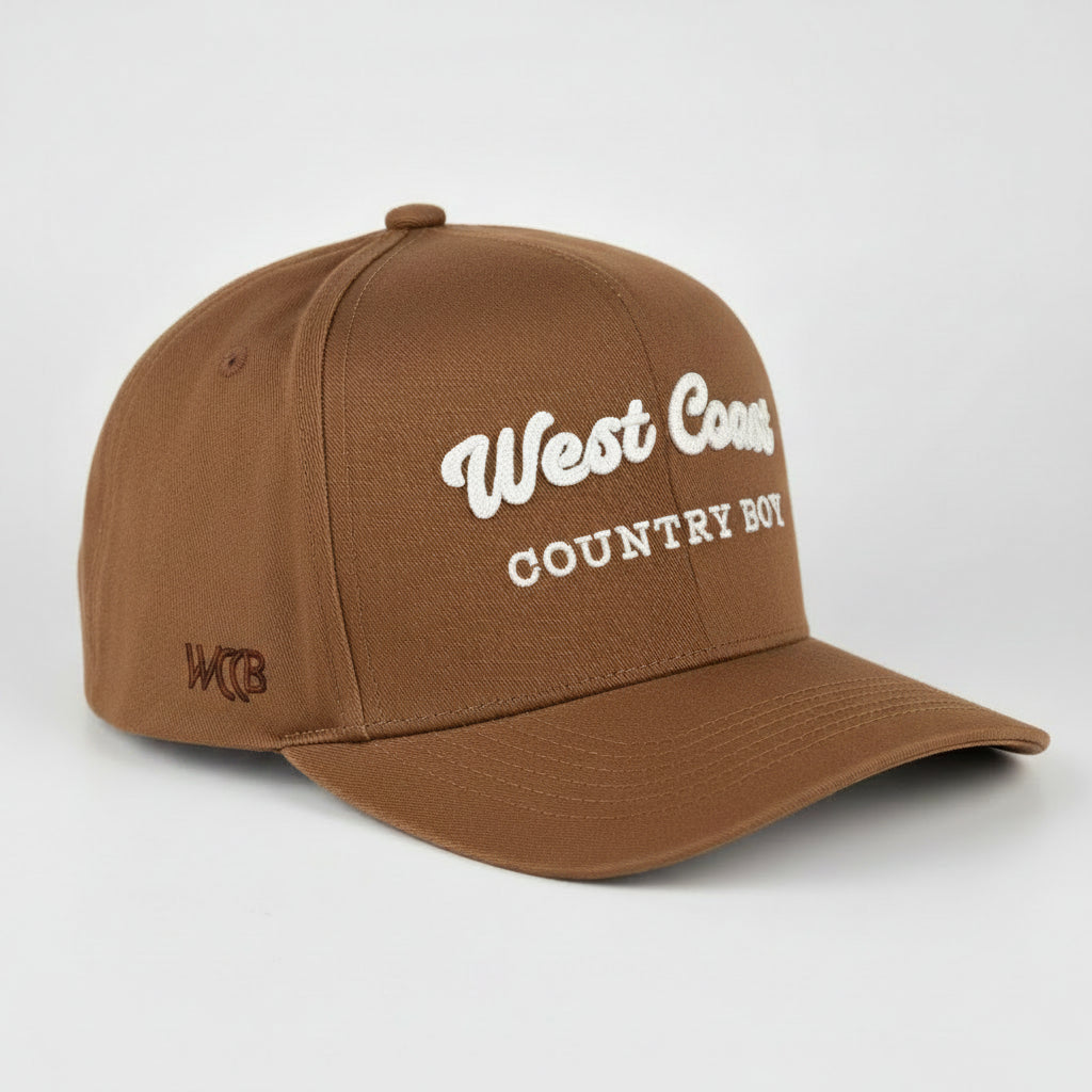 A royal blue baseball cap with 'West Coast COUNTRY BOY' embroidered in white on the front, shown on a light gray studio background.